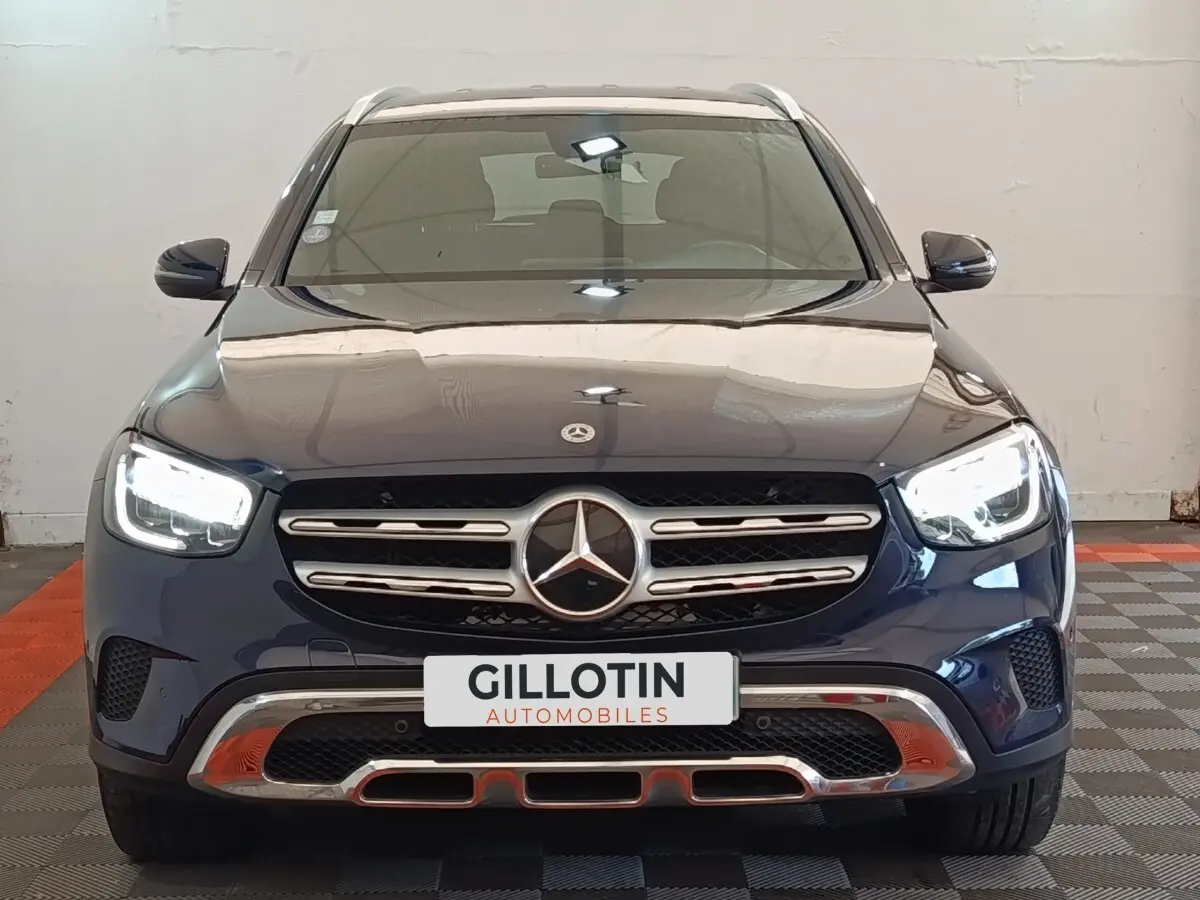 Vue frontale d'un Mercedes GLC 300 DE Business Line hybride rechargeable bleu avec calandre chromée et phares LED allumés.