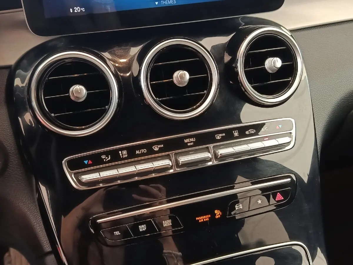 Gros plan sur la console centrale noire brillante du Mercedes GLC 300 hybride, avec aérateurs ronds et commandes climatisation.