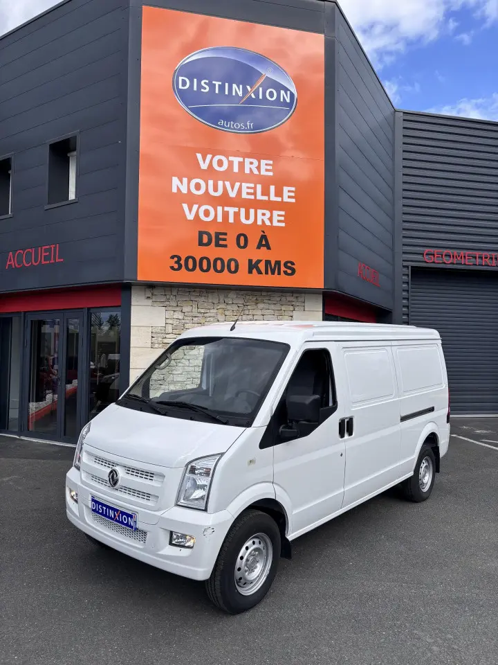 Vue 3/4 avant droit du fourgon blanc DFSK EC35 SERES ECOCITY 2023 devant un bâtiment commercial.