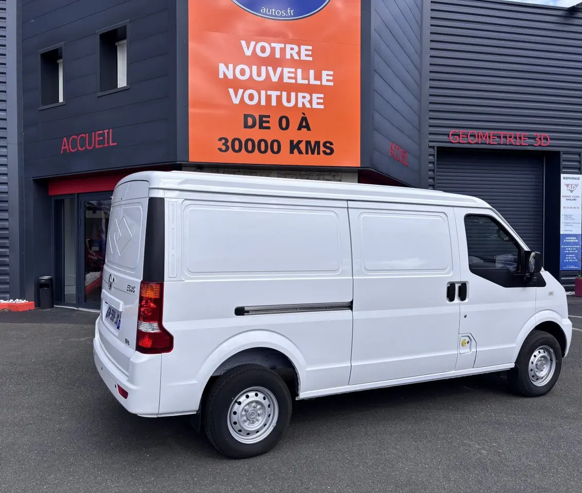 Vue 3/4 arrière côté droit du fourgon électrique blanc DFSK EC35 Seres Ecocity 2023 stationné devant un bâtiment.