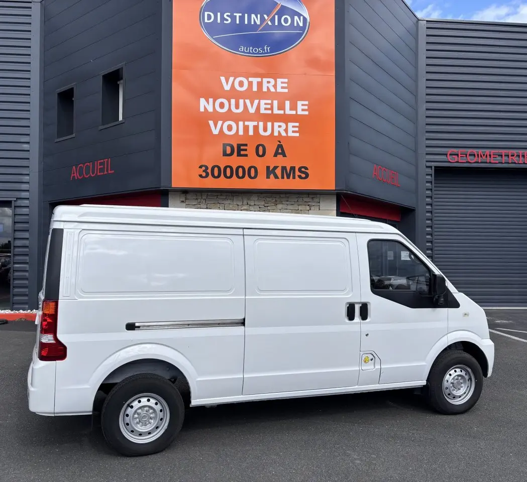 Vue latérale droite d'un utilitaire blanc DFSK EC35 SERES ECOCITY 2023 garé devant un bâtiment commercial.