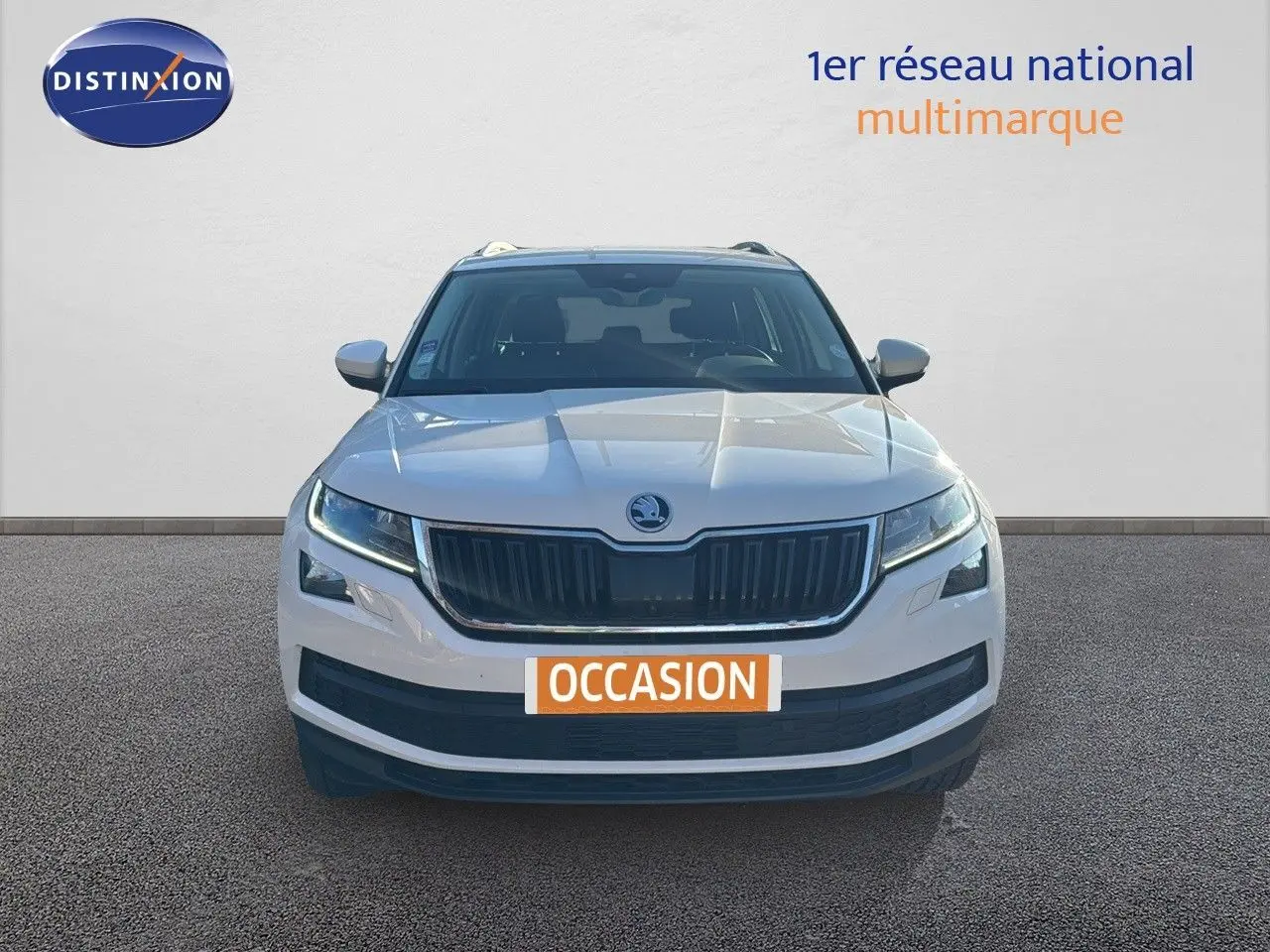 Vue frontale d'un Skoda Kodiaq blanc 2018 avec calandre noire et feux LED allumés sur fond neutre.