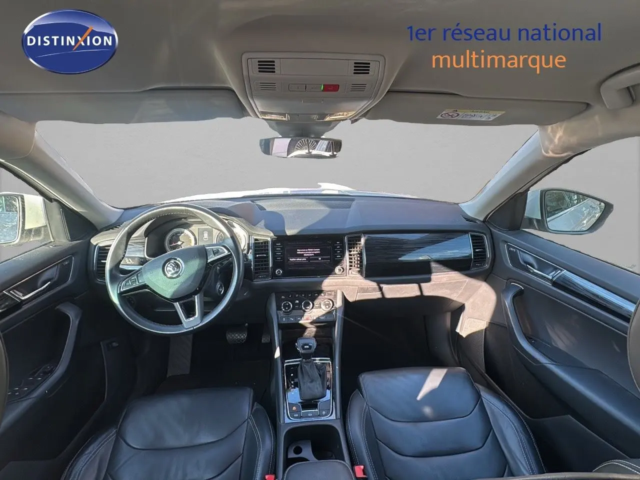 Intérieur du Skoda Kodiaq blanc 2018 vu de face, tableau de bord moderne avec volant multifonction et sièges cuir noir.