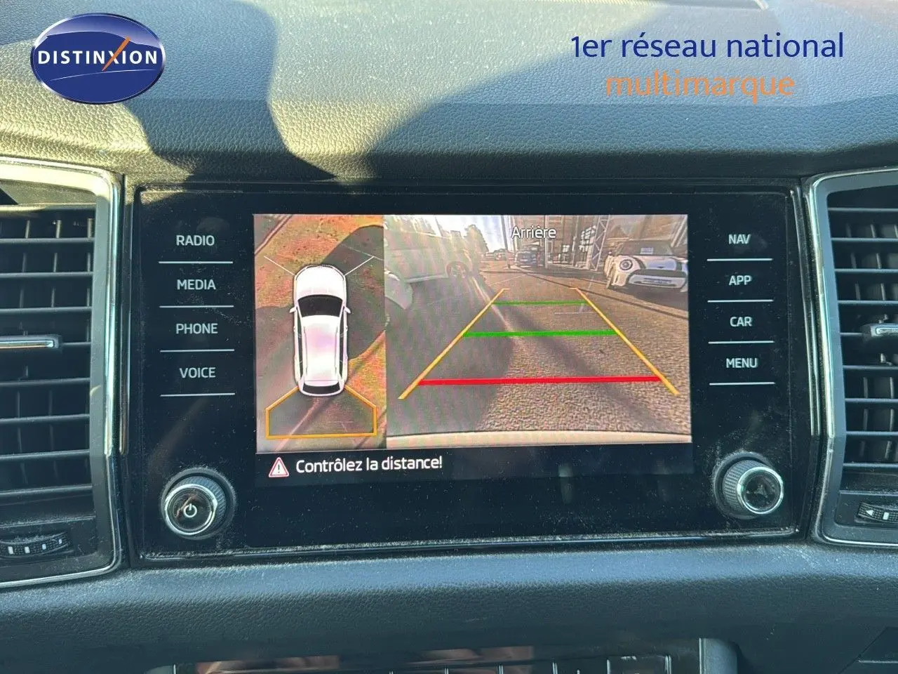 Écran central du Skoda Kodiaq blanc montrant la caméra de recul avec vue arrière et top-down du véhicule.