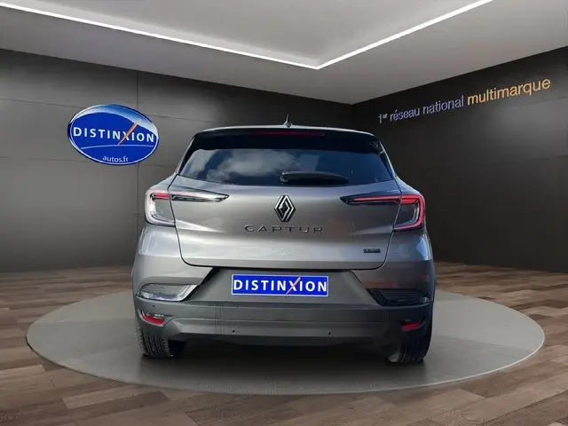 Vue arrière du Renault Captur 2025 gris Cassiopée avec toit noir et logo distinctif dans un showroom.