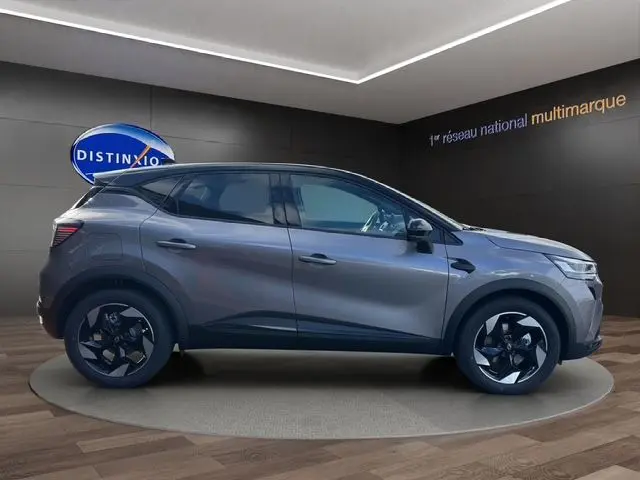 Profil droit du Renault Captur 2025 gris Cassiopée avec toit noir, roues noires et peinture bi-ton, en intérieur showroom.