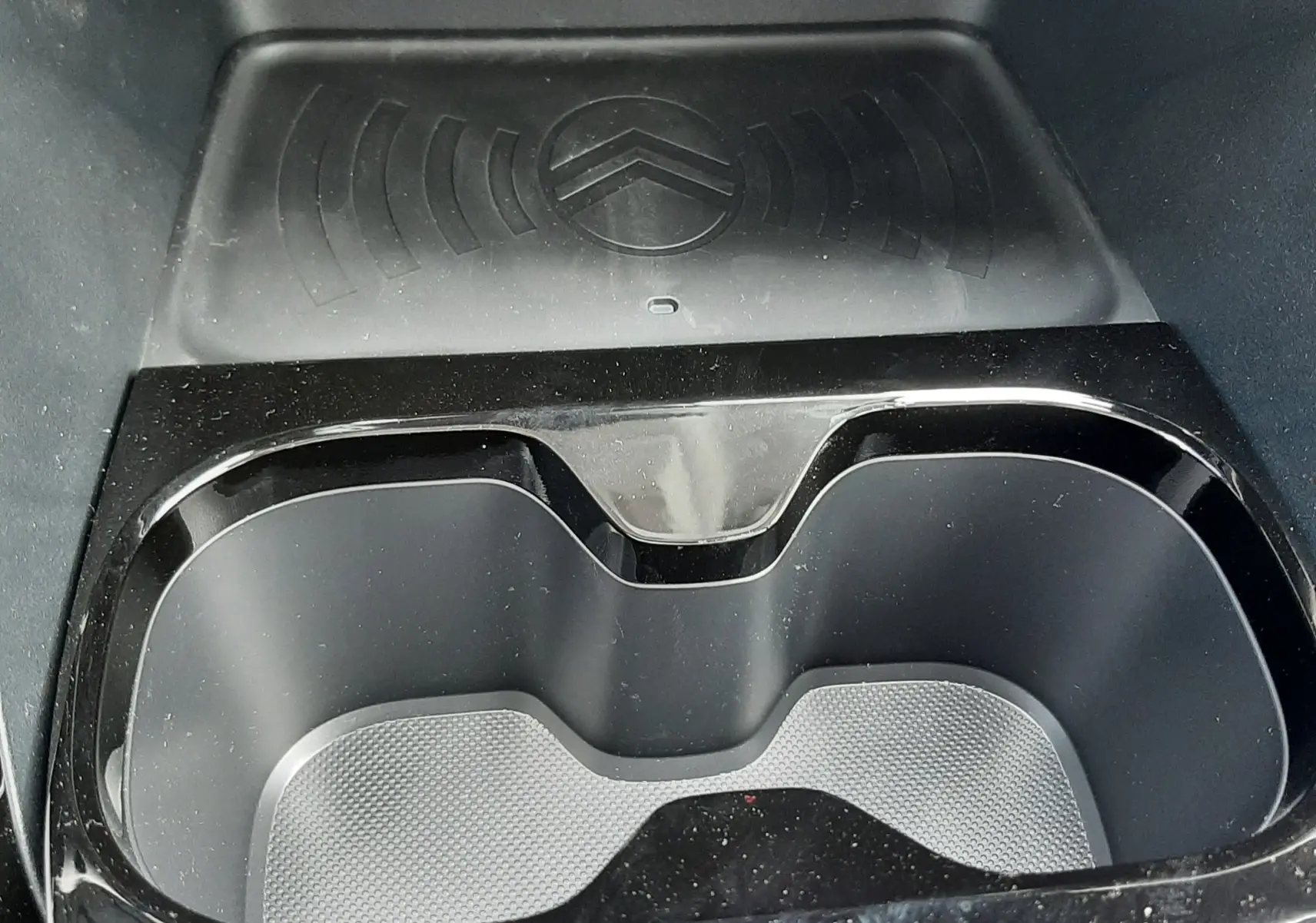 Gros plan intérieur sur le porte-gobelets noir brillant et le chargeur sans fil avec logo Citroën du Citroën C3 Aircross blanc banquise.