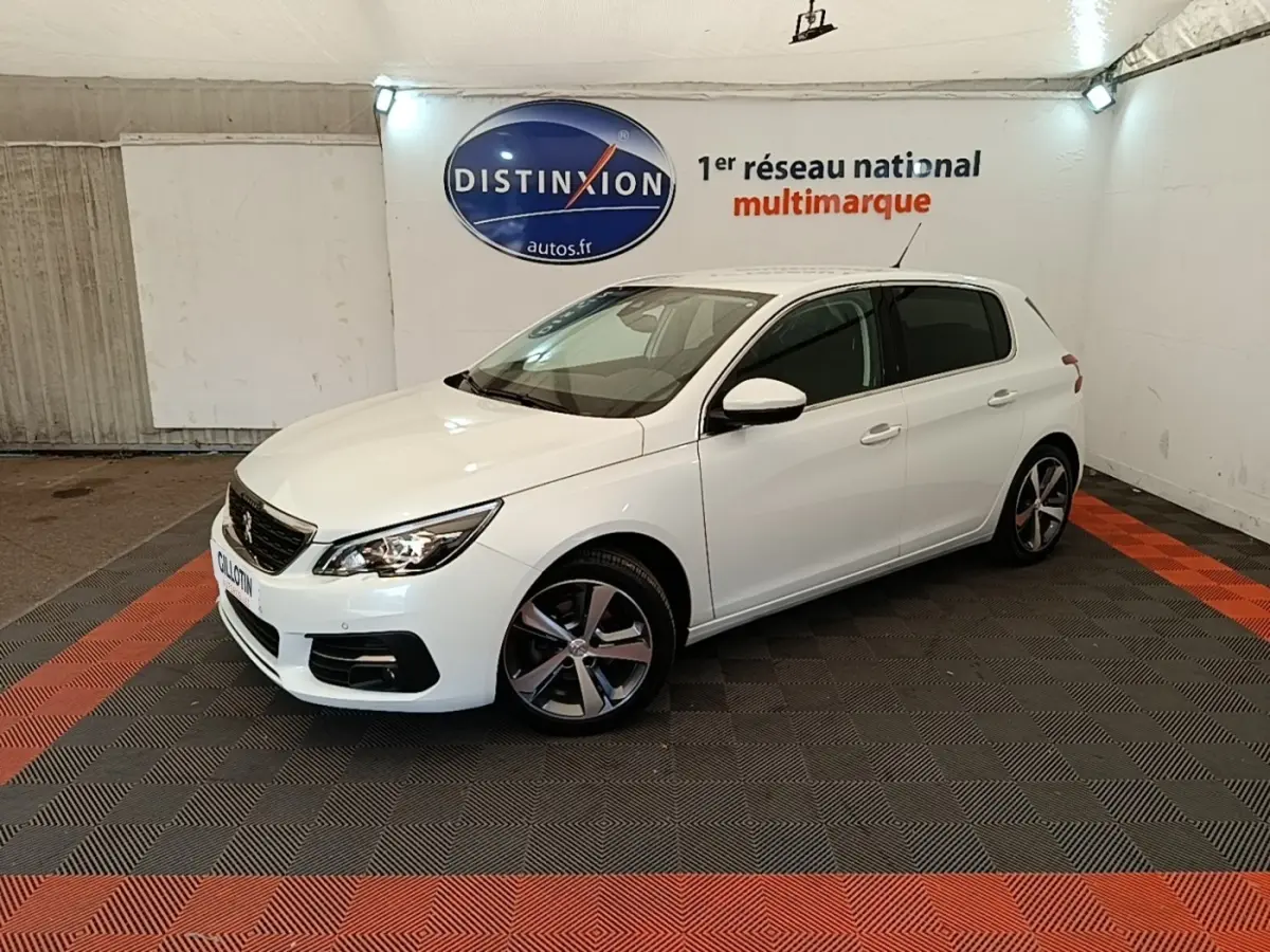 Peugeot 308 blanc vue 3/4 avant droit dans un showroom avec jantes alliage et phares allumés.