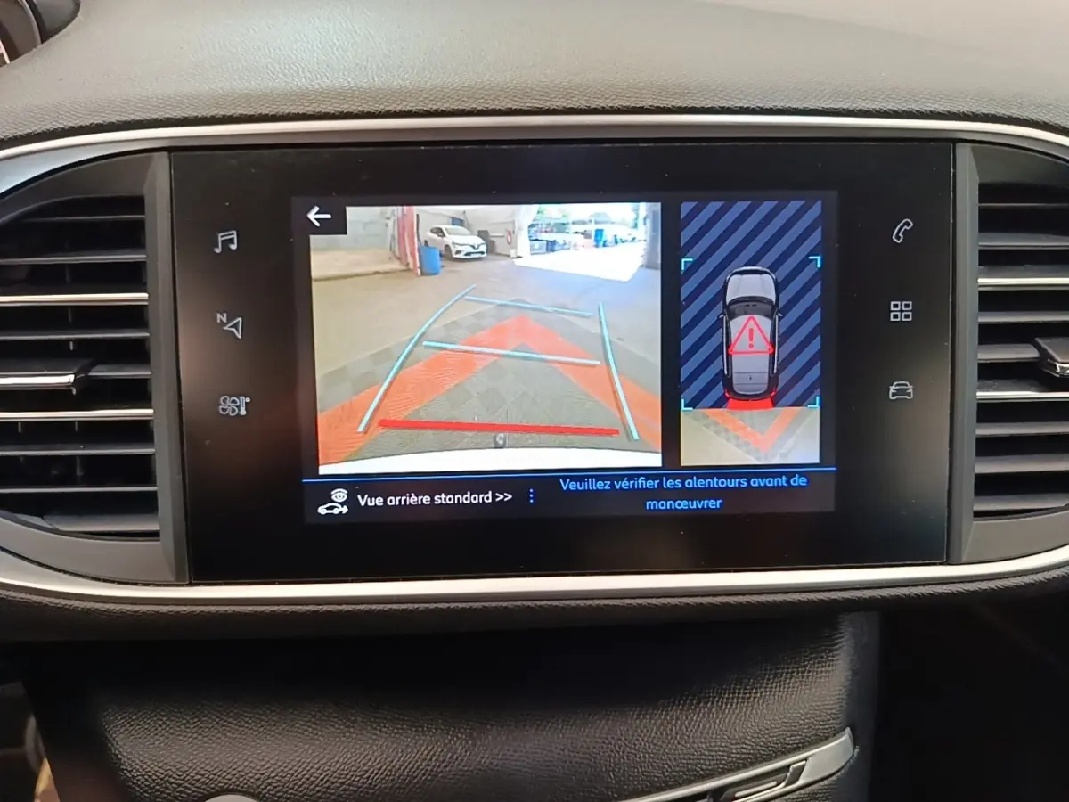 Écran tactile intérieur de la Peugeot 308 blanc montrant la caméra de recul et l'alerte de proximité arrière.