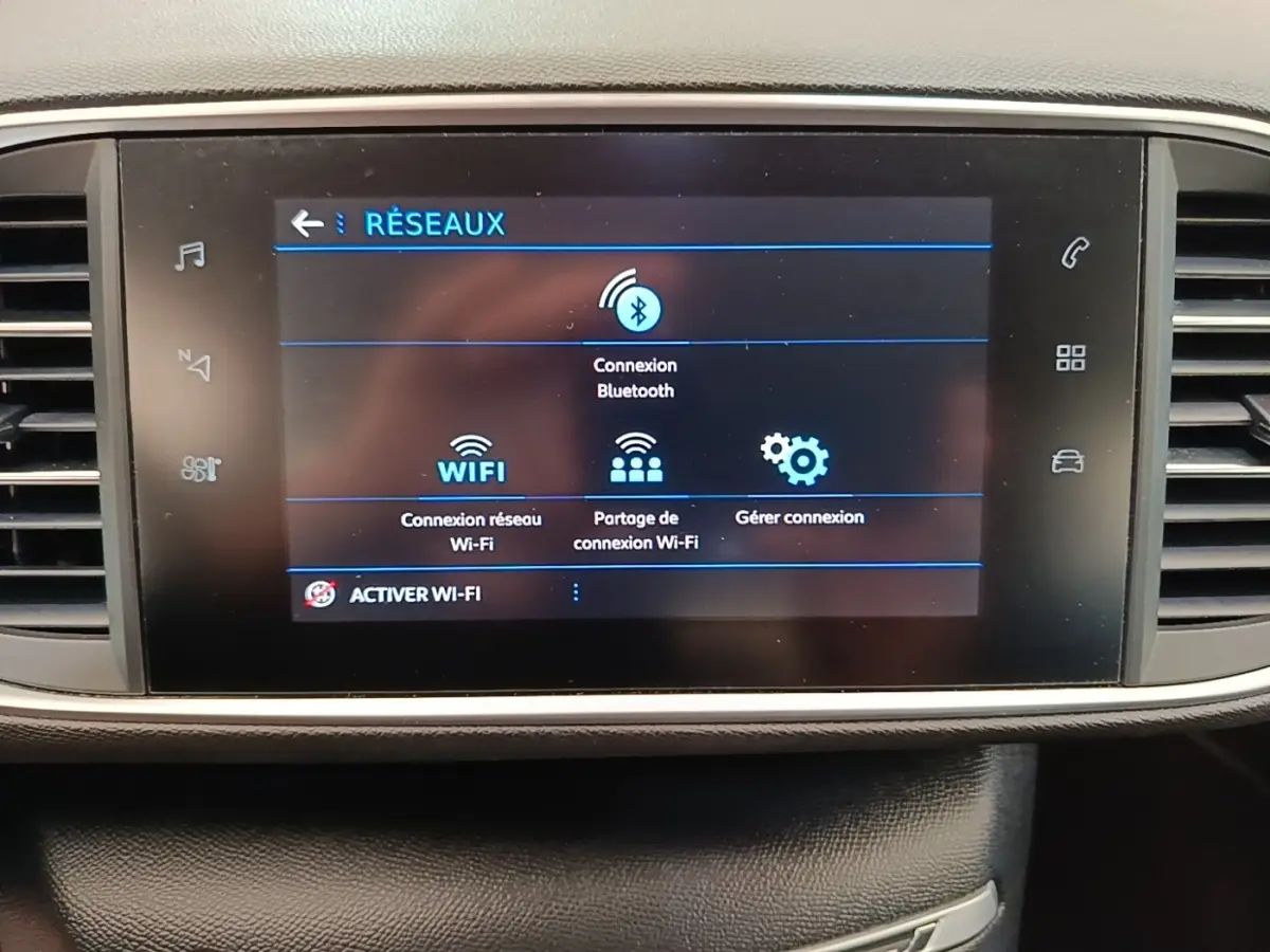 Écran tactile central de la Peugeot 308 blanc, affichant le menu de connexion Bluetooth et Wi-Fi, intérieur noir.