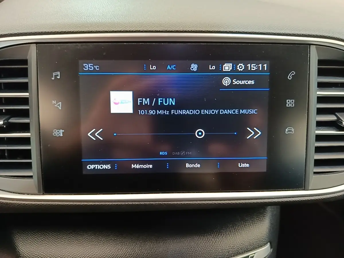 Écran tactile central de la Peugeot 308 blanc, affichant la radio FM avec interface moderne et commandes tactiles.
