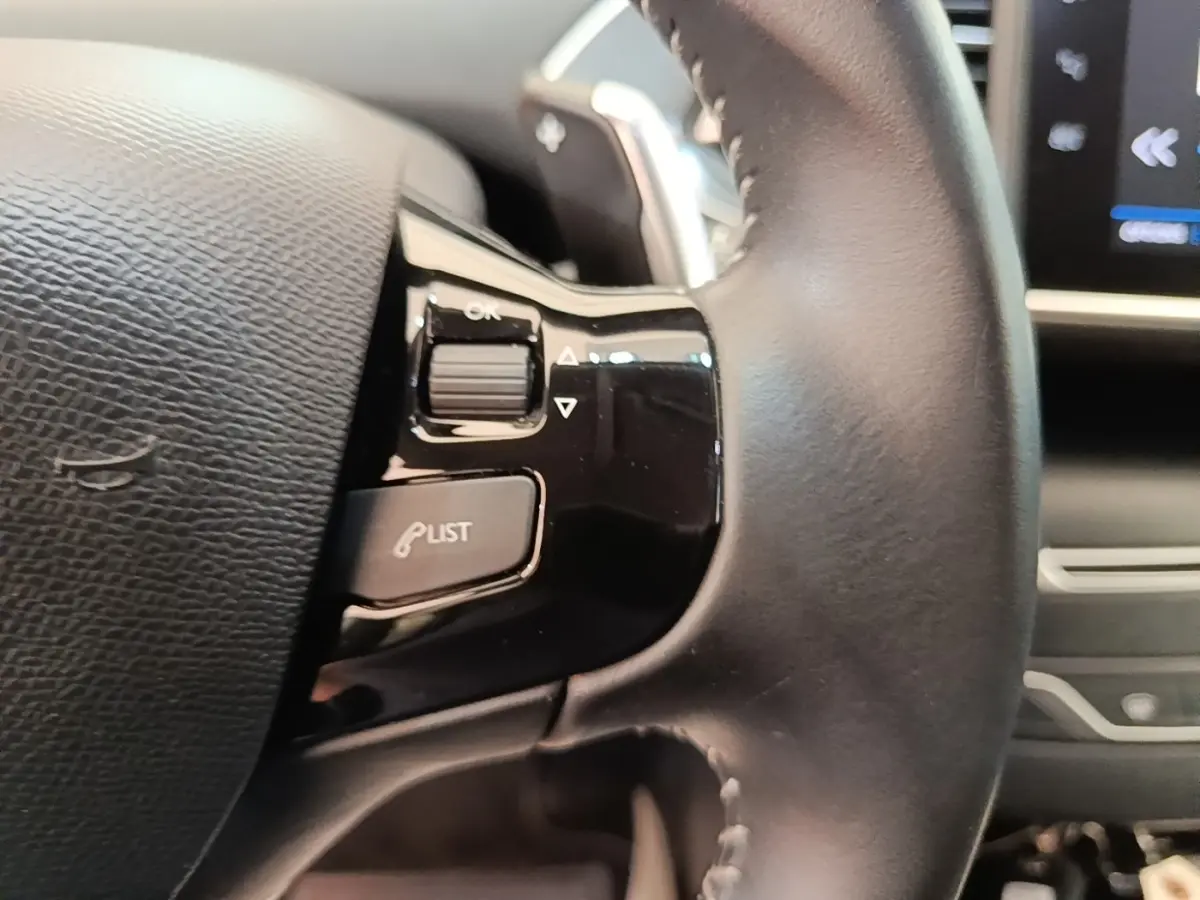 Gros plan sur le volant cuir noir de la Peugeot 308 2020 avec commandes multifonctions et écran tactile en arrière-plan.