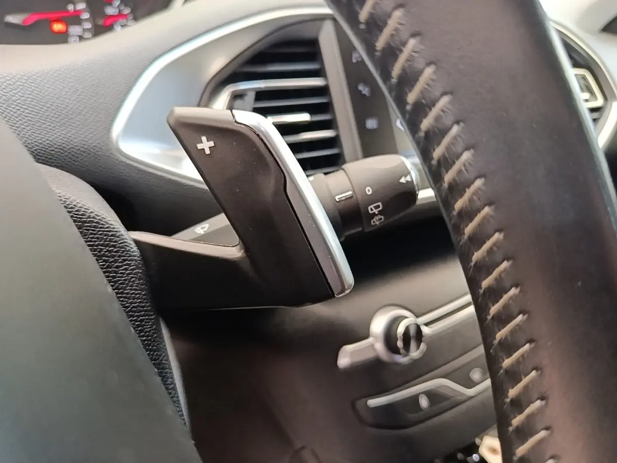 Gros plan sur la palette de changement de vitesse droite et partie du volant cuir noir du Peugeot 308 blanc, intérieur.