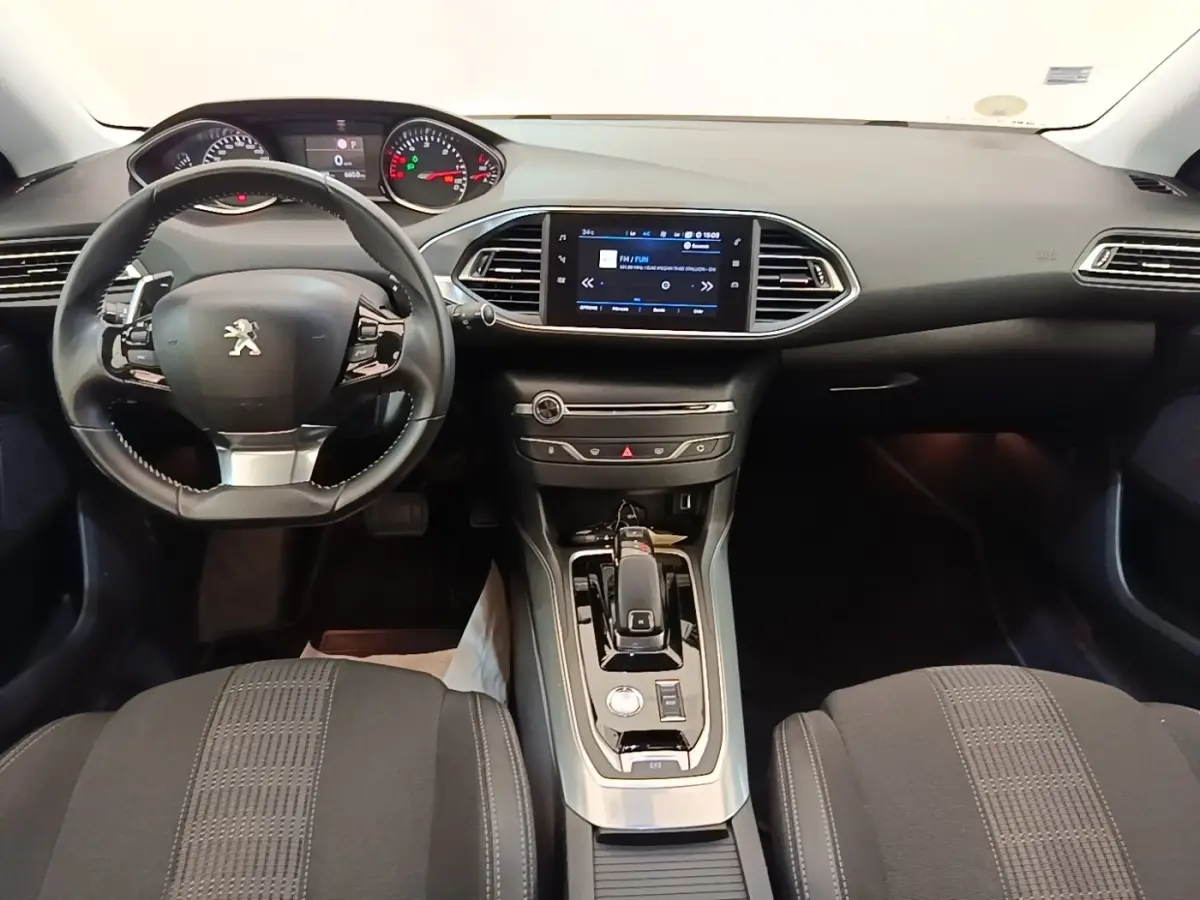 Vue intérieure avant de la Peugeot 308 blanche, tableau de bord avec écran tactile et volant cuir multifonctions.