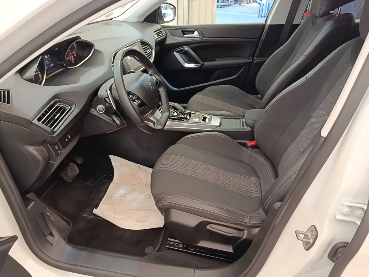 Intérieur avant droit d’une Peugeot 308 blanche, sièges noirs, volant cuir multifonctions et tableau de bord moderne.
