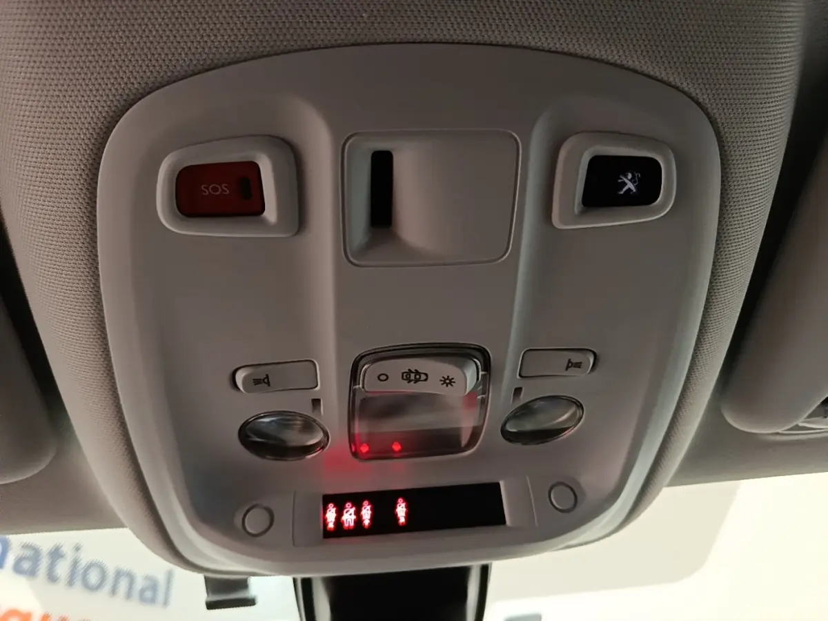 Vue intérieure en gros plan du plafonnier de la Peugeot 308 blanc, avec boutons SOS et éclairage, et témoins rouges allumés.