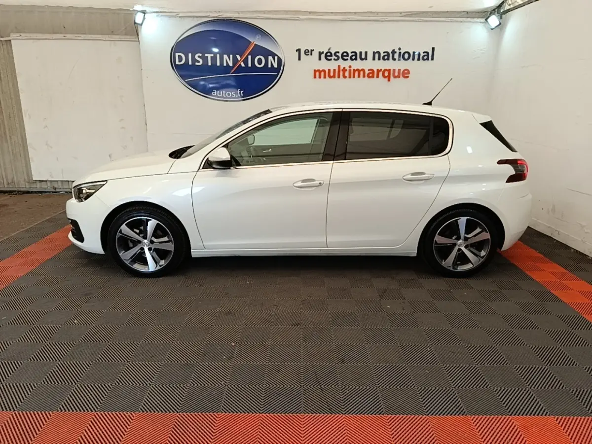 Profil latéral droit d'une Peugeot 308 blanche 2020 dans un showroom avec sol gris et rouge.