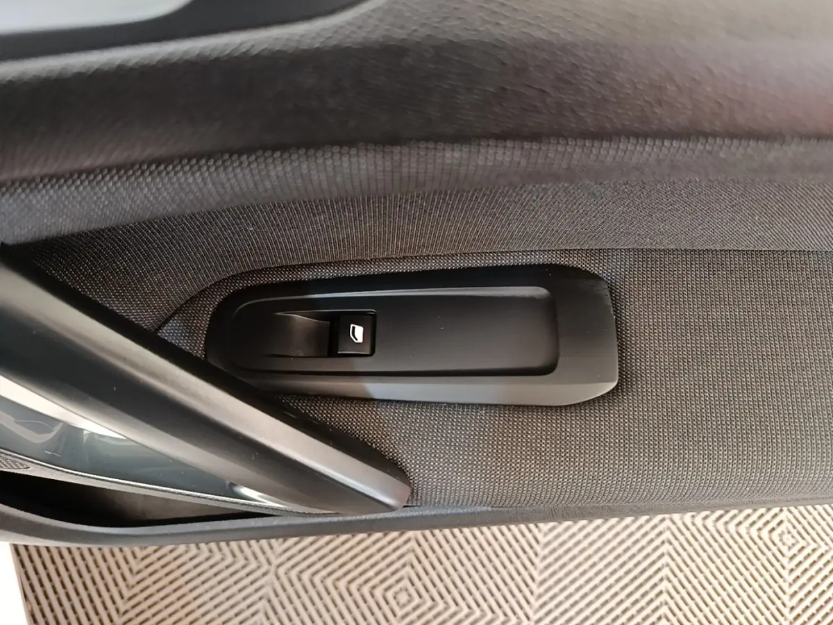 Détail de la commande de lève-vitre électrique sur la porte intérieure côté gauche d’une Peugeot 308 blanche.