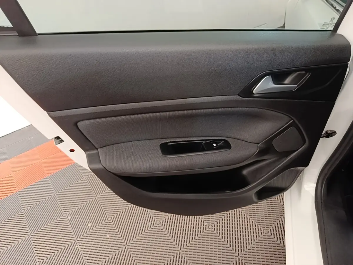 Vue intérieure de la porte avant gauche d'une Peugeot 308 blanche, avec garniture noire et commande de vitre électrique.