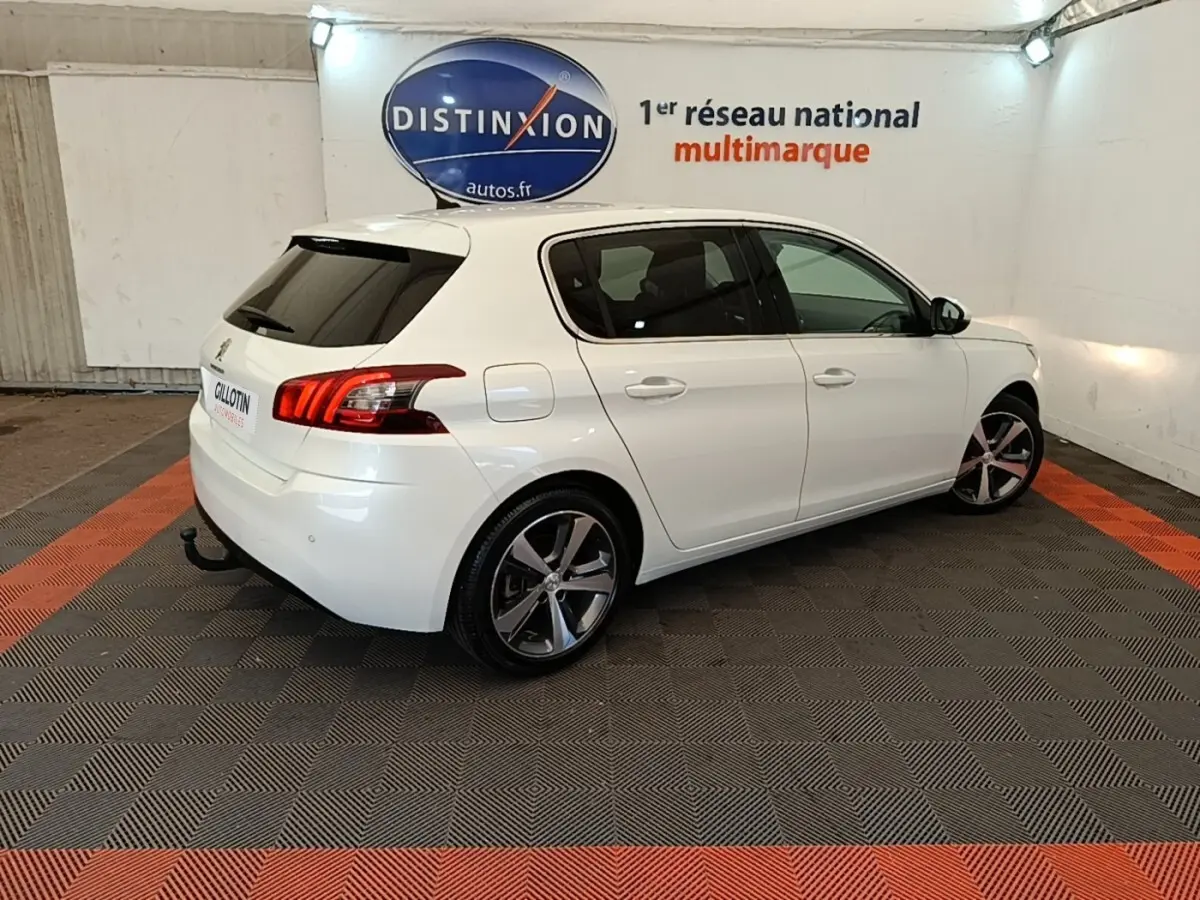 Vue 3/4 arrière droite d'une Peugeot 308 blanche en intérieur, avec jantes alliage et feux arrière LED distinctifs.
