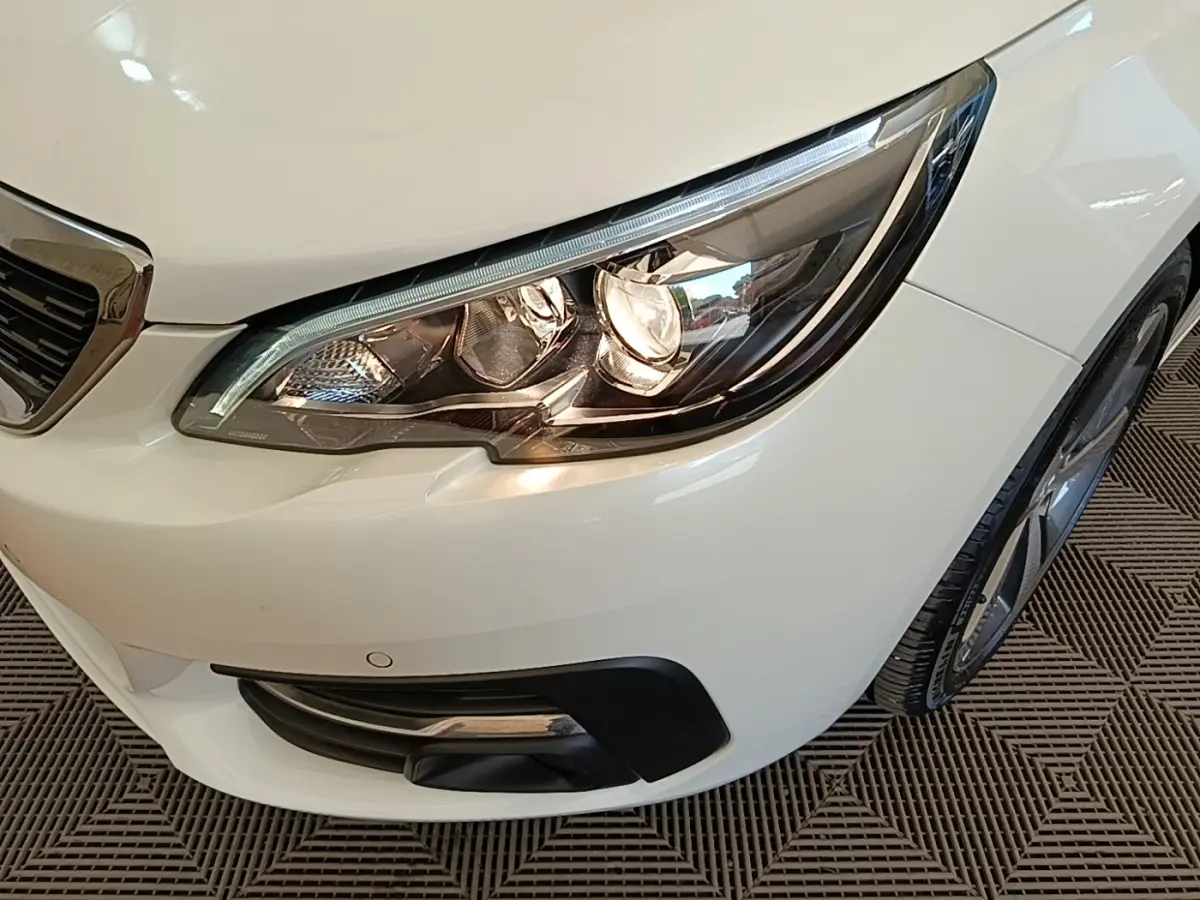 Gros plan sur le phare avant droit blanc d’une Peugeot 308 avec calandre chromée et antibrouillard intégré.