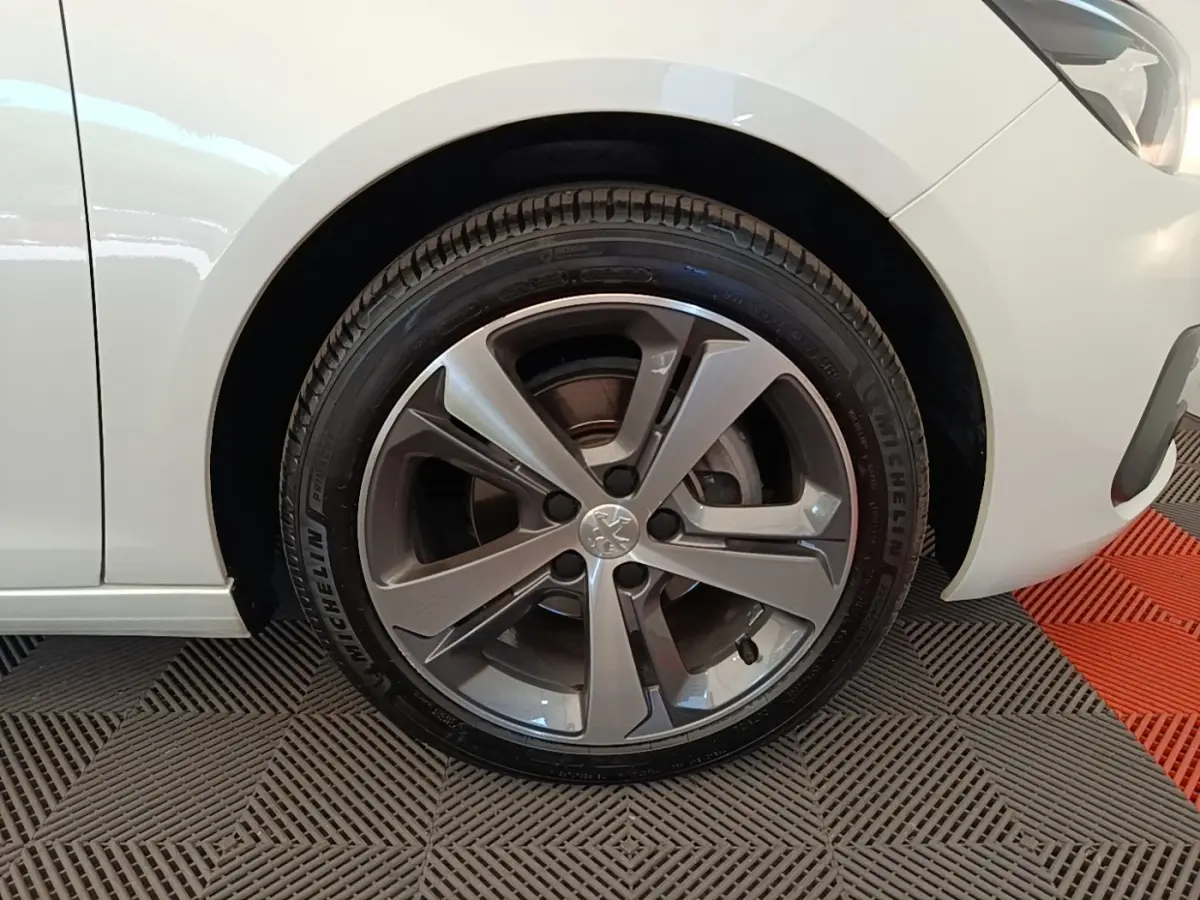 Gros plan sur la roue avant droite d'une Peugeot 308 blanche, jante alliage gris foncé, pneu Michelin visible.