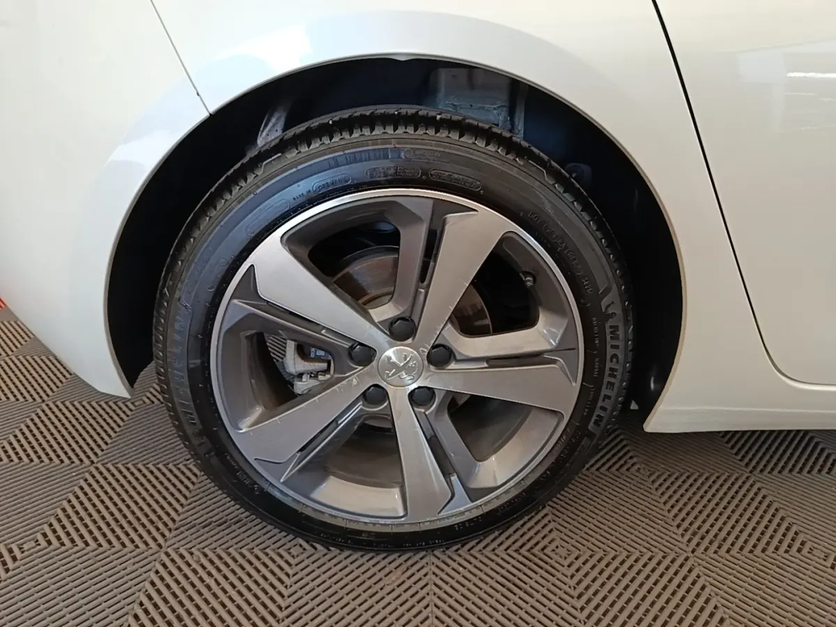 Gros plan sur la roue arrière droite d'une Peugeot 308 blanche, avec jante alliage gris foncé et pneu Michelin.
