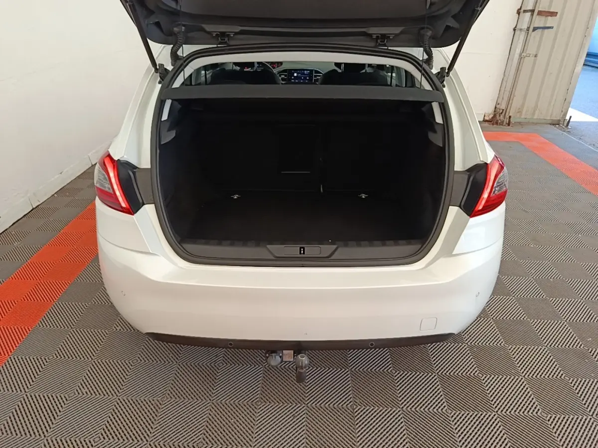 Vue arrière ouverte d'une Peugeot 308 blanche montrant le coffre spacieux et l'attelage de remorque.