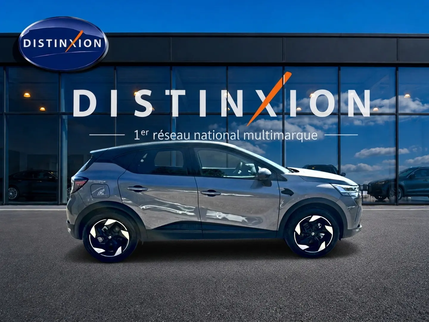 Profil droit du Renault Captur gris cassiopée 2026 devant une vitrine avec logo Distinxion.