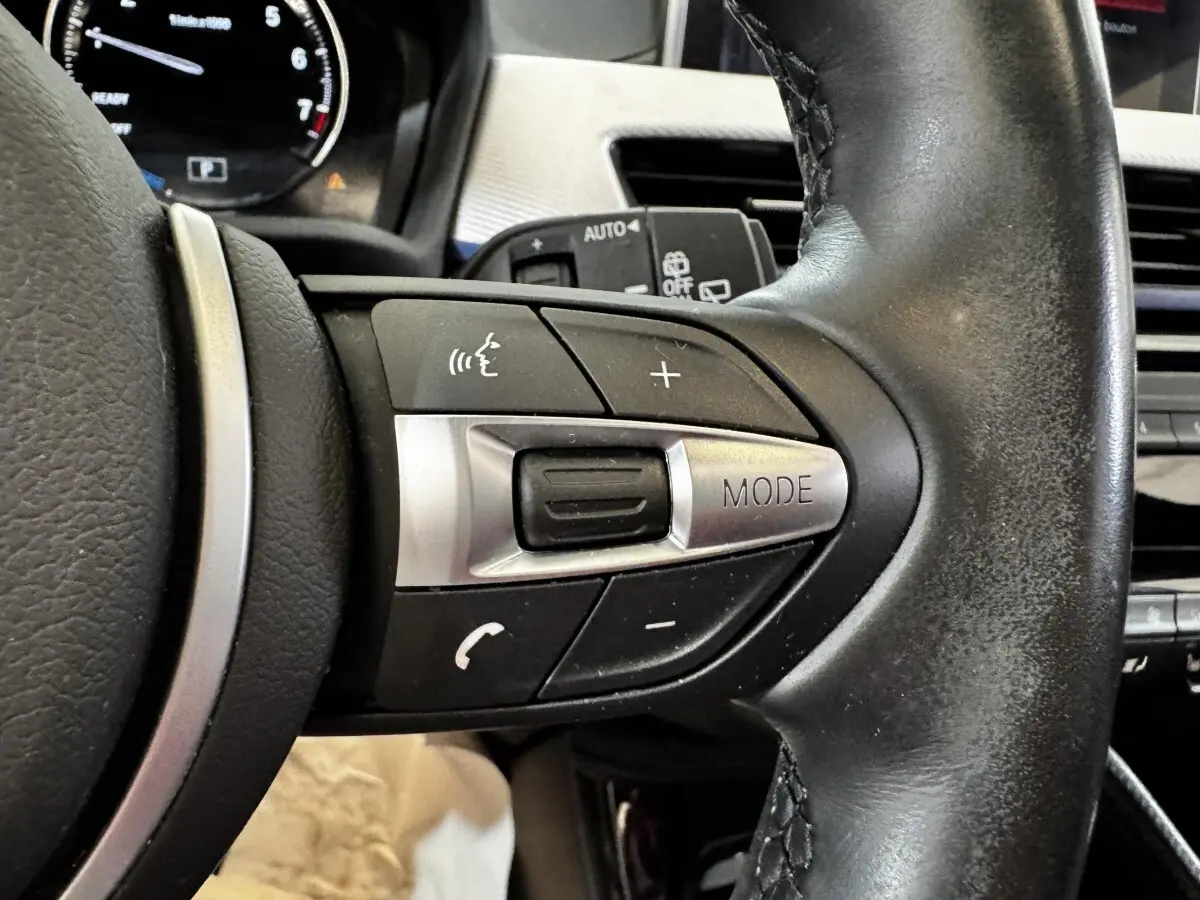 Gros plan sur les commandes multifonctions en cuir et aluminium du volant du BMW X2 xDrive25e blanc de 2022.