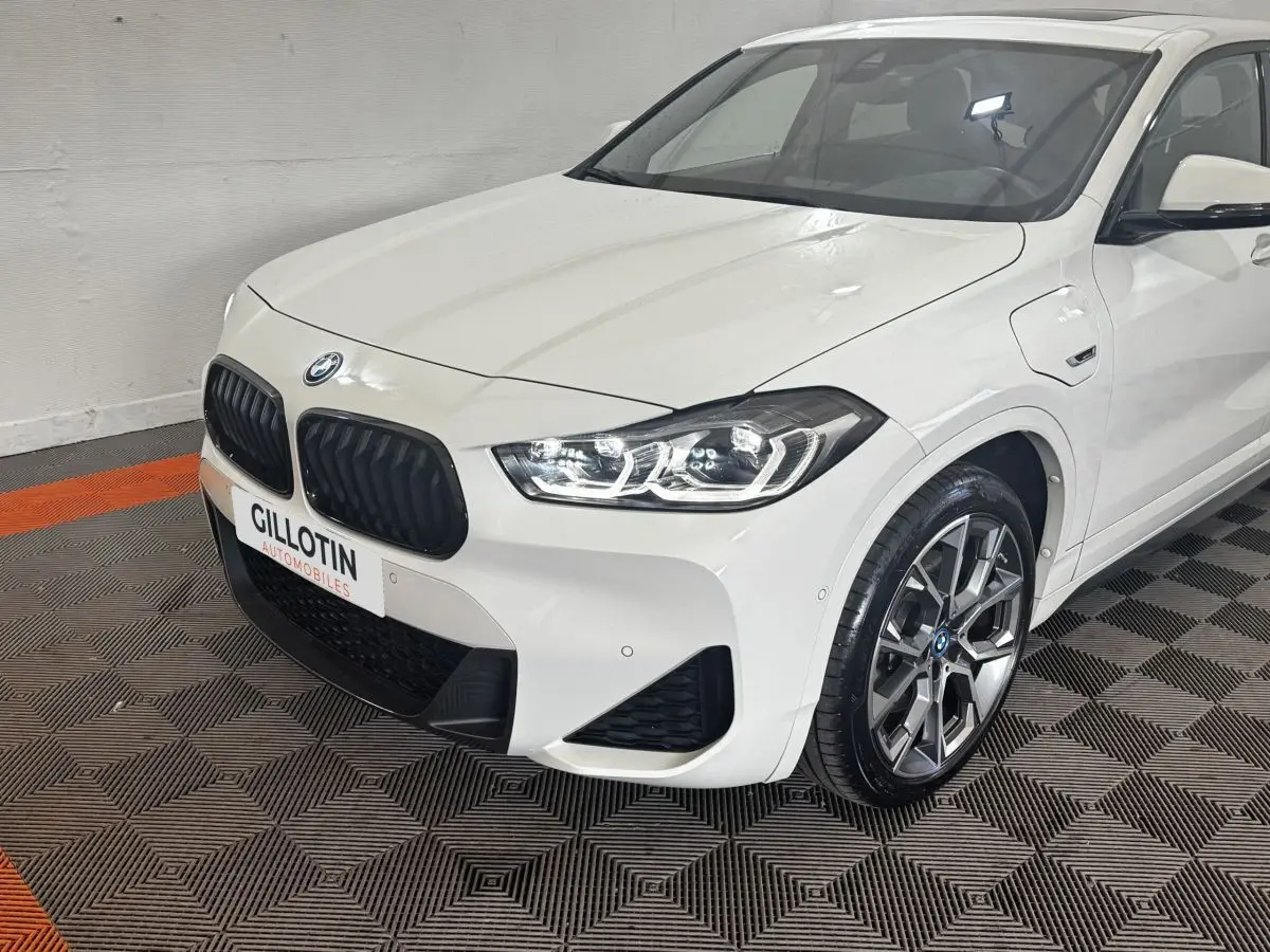 BMW X2 xDrive25e blanc vue 3/4 avant droit, calandre noire et jantes alliage distinctives.