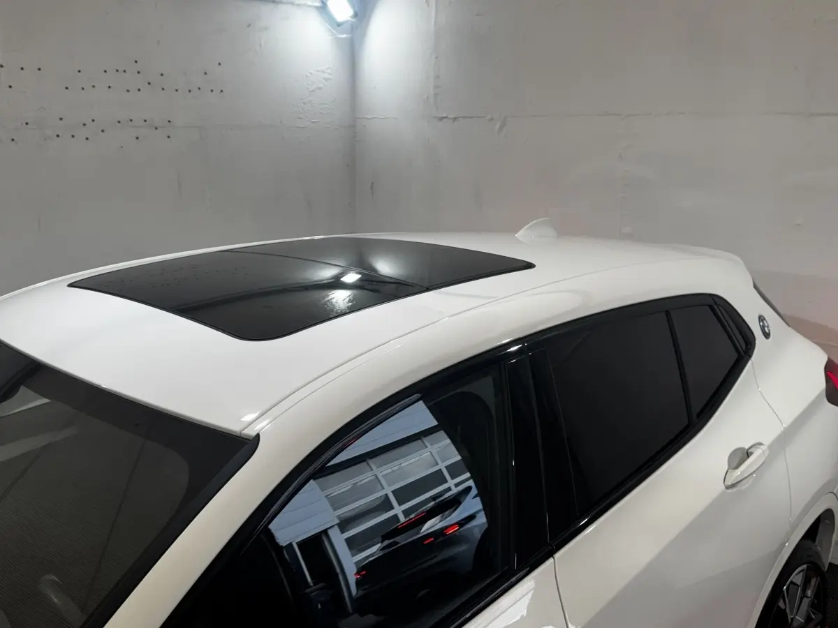Vue 3/4 arrière droite d’un BMW X2 blanc avec toit panoramique noir et vitres teintées dans un garage.