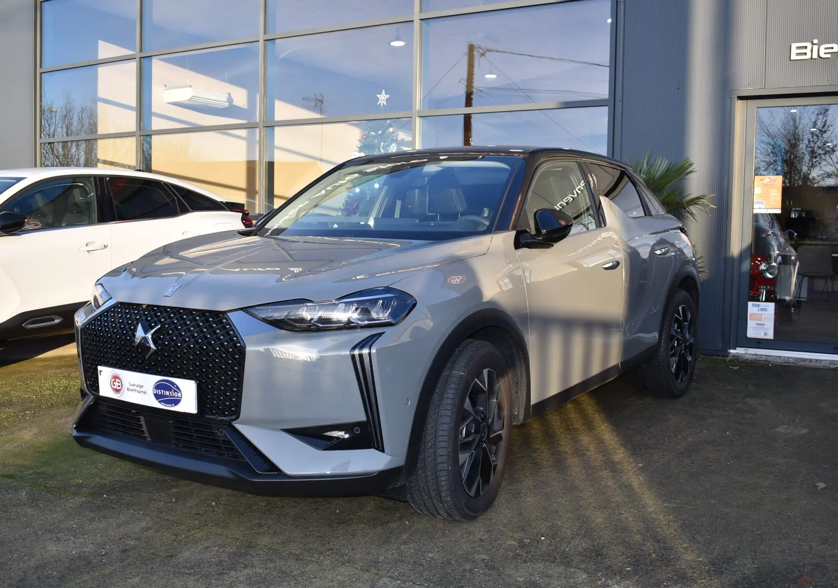 DS3 Crossback gris 3/4 avant droit avec toit noir, calandre distinctive et jantes noires, devant un showroom.