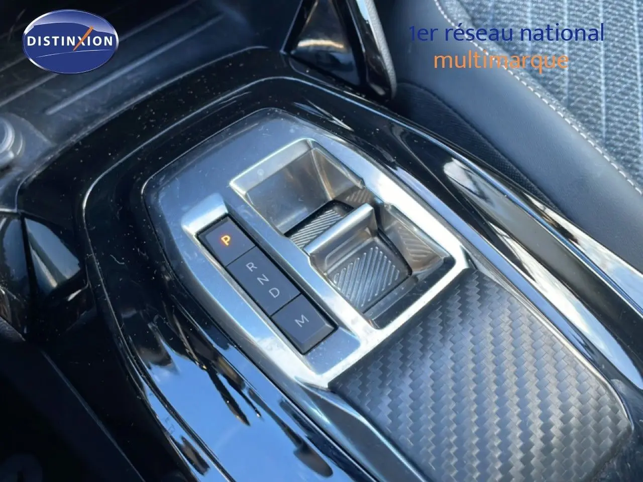 Gros plan sur la console centrale noire de la Peugeot 208 hybride 2025 avec sélecteur de boîte automatique et finition carbone.