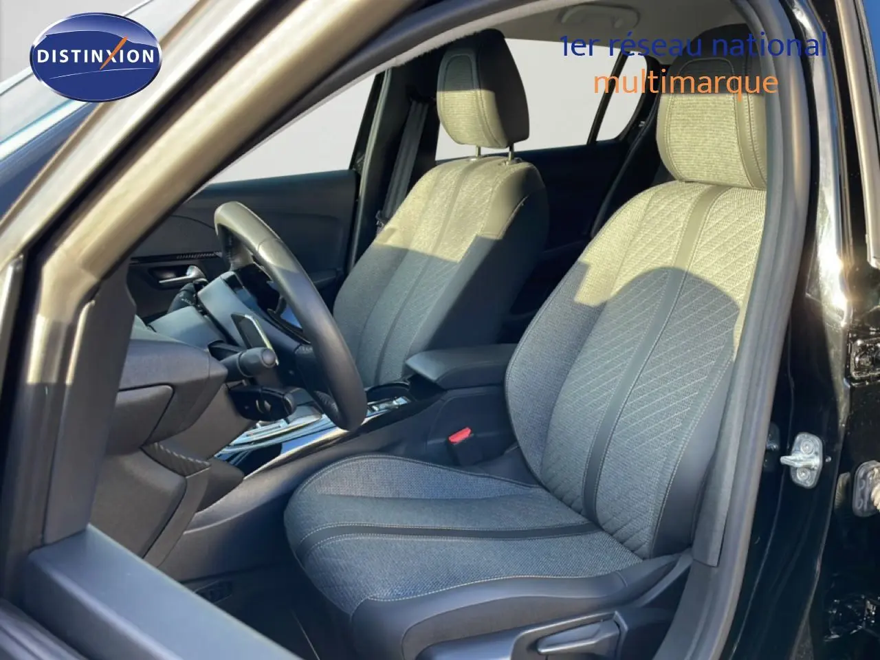 Vue intérieure côté conducteur de la Peugeot 208 noire 2025, sièges tissu gris avec détails cuir et volant multifonction.