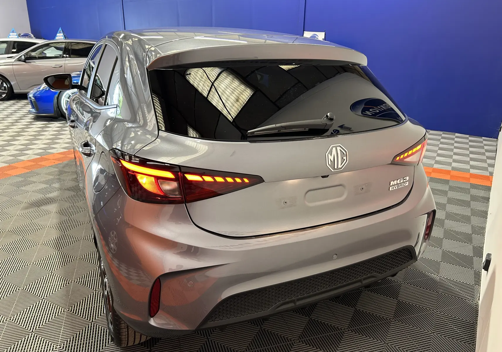 Vue 3/4 arrière droite d'une MG3 hybride gris Hampstead avec feux arrière allumés dans un showroom.