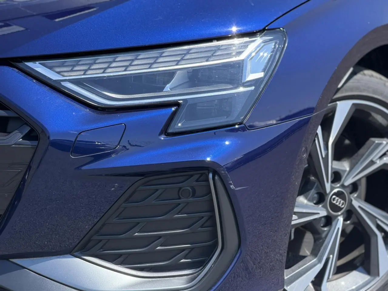 Gros plan sur l'avant droit bleu Navarre de l'Audi A3 Sportback 2025, mettant en valeur le phare Matrix LED et la jante alliage.