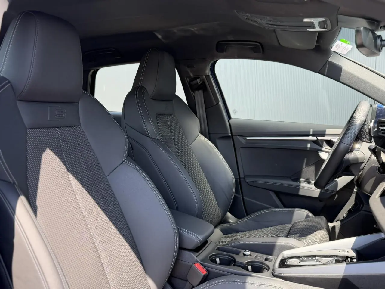 Vue intérieure côté droit des sièges sport noirs avec surpiqûres blanches et volant cuir de l'Audi A3 Sportback S-Line 2025.