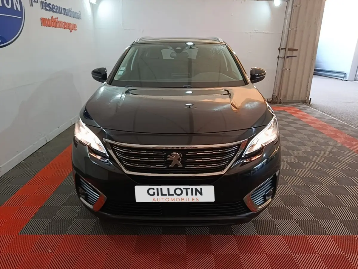 Peugeot 5008 noir vue de face, phares allumés, calandre chromée et logo lion visible, intérieur clair.