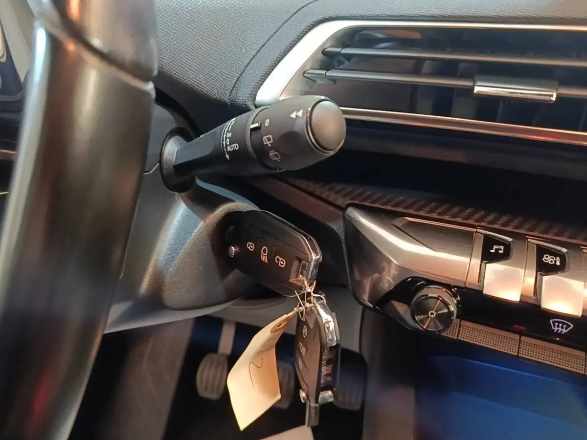 Gros plan intérieur sur le volant et la clé de contact du Peugeot 5008 noir, avec commandes et tableau de bord partiellement visibles.