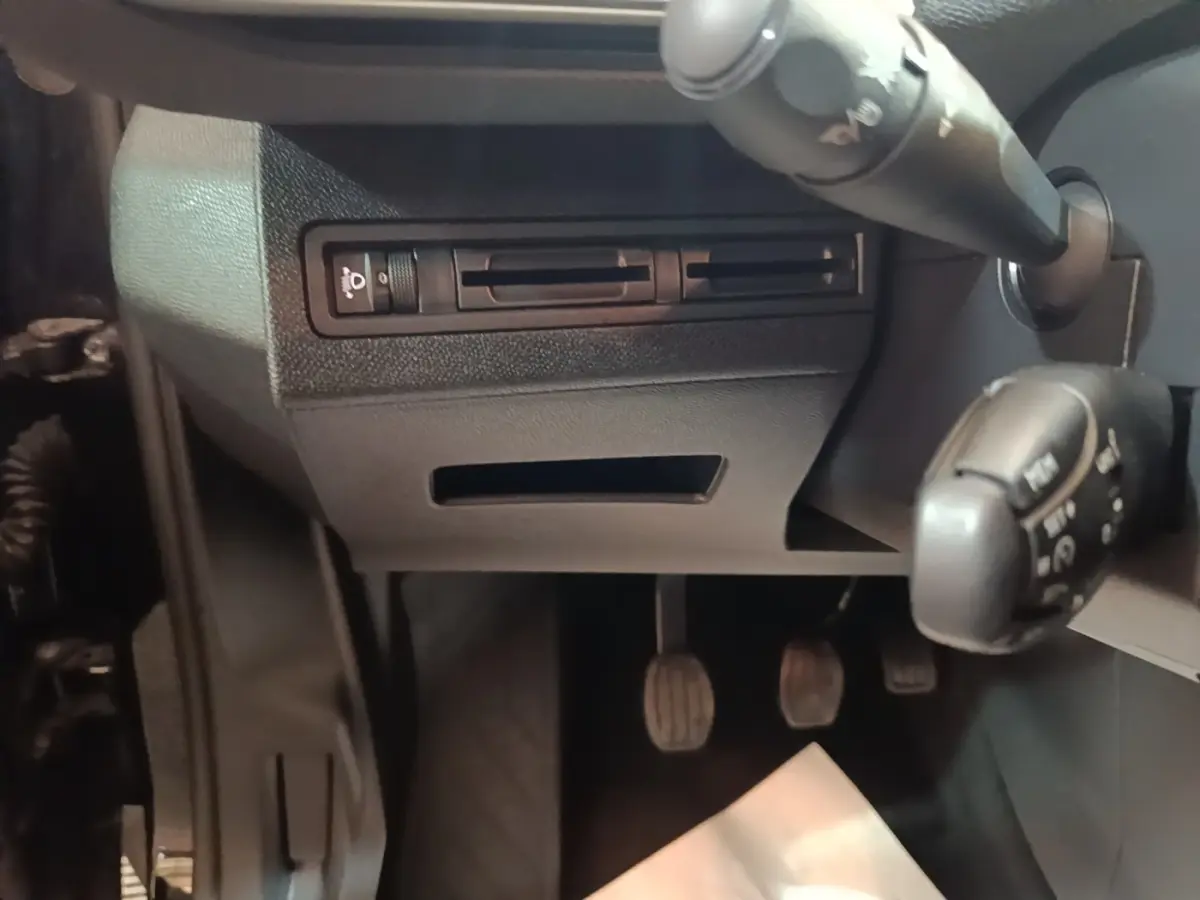 Détail de la partie inférieure du tableau de bord côté conducteur du Peugeot 5008 noir, avec pédales et commandes au volant visibles.
