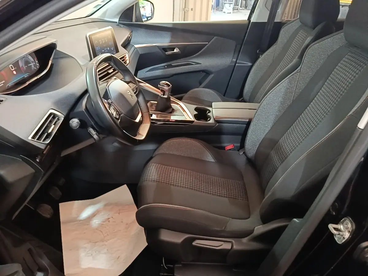 Intérieur avant droit du Peugeot 5008 noir, montrant sièges tissu, volant cuir multifonctions et tableau de bord digital.