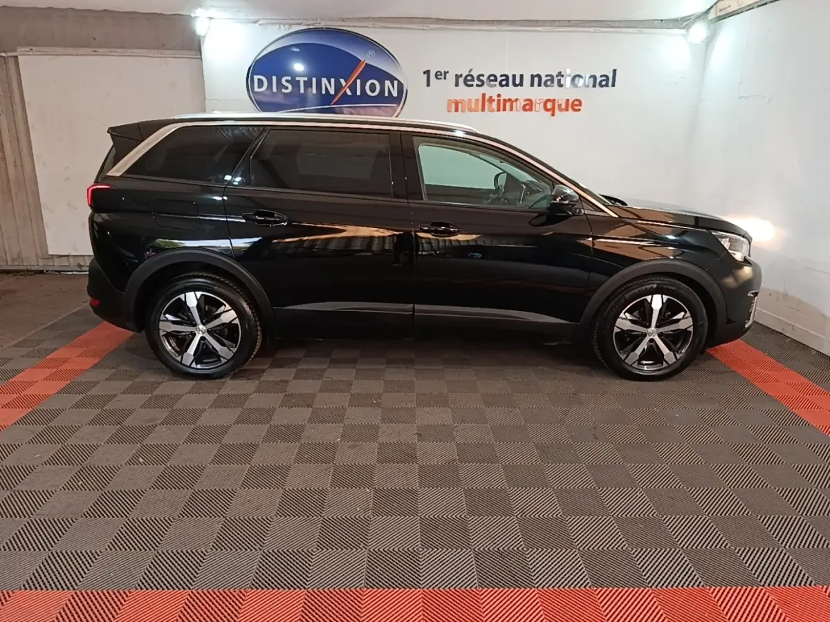 Peugeot 5008 noir vue de profil côté gauche dans un showroom avec jantes alliage et vitres teintées.