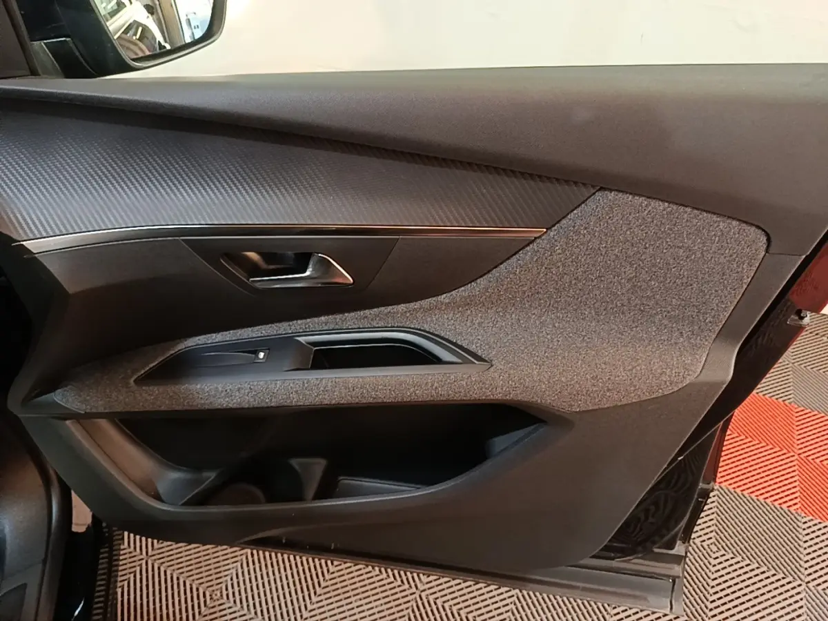 Vue intérieure côté gauche de la porte avant d’un Peugeot 5008 noir avec garniture tissu et plastique noir.