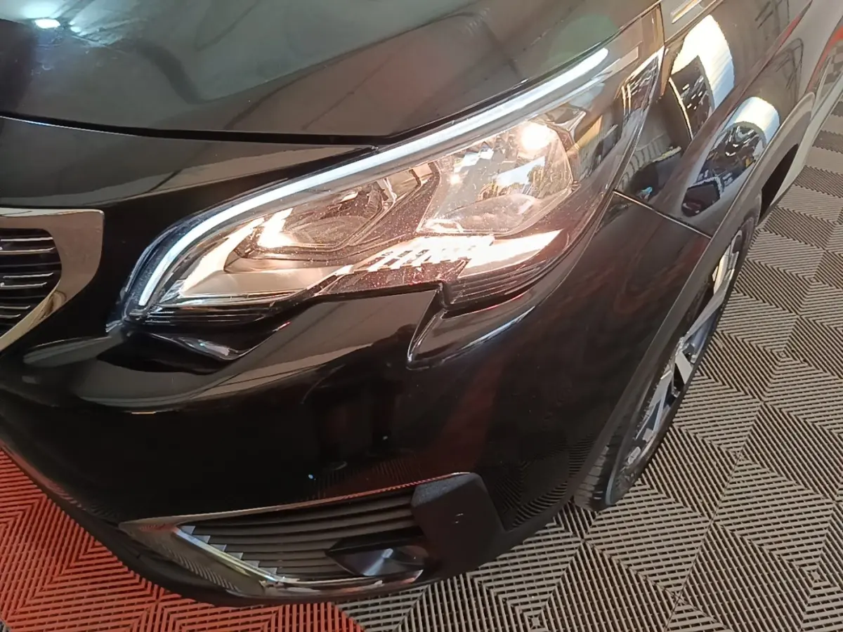 Gros plan sur le phare avant droit d’un Peugeot 5008 noir, avec partie de la calandre et roue visible.