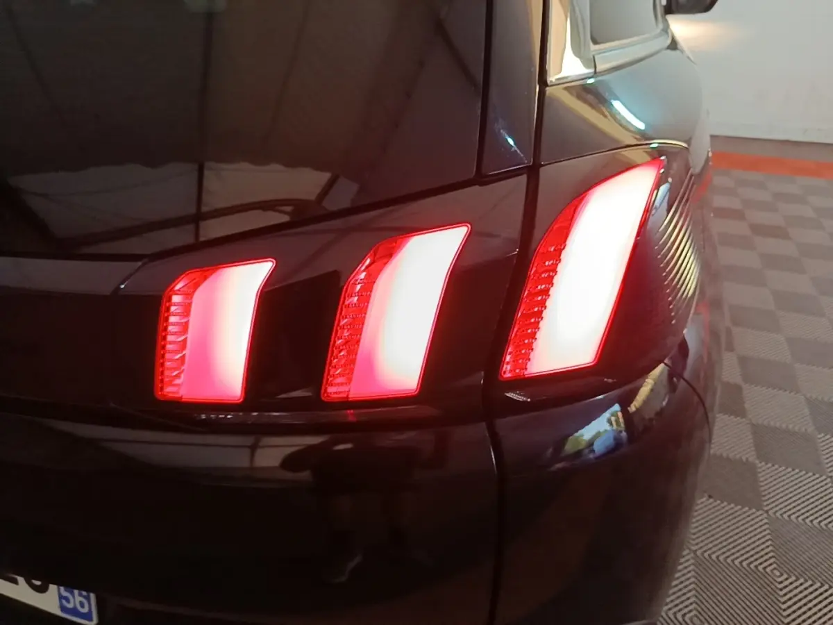 Gros plan sur le feu arrière droit rouge allumé d’un Peugeot 5008 noir, avec reflet sur la carrosserie brillante.
