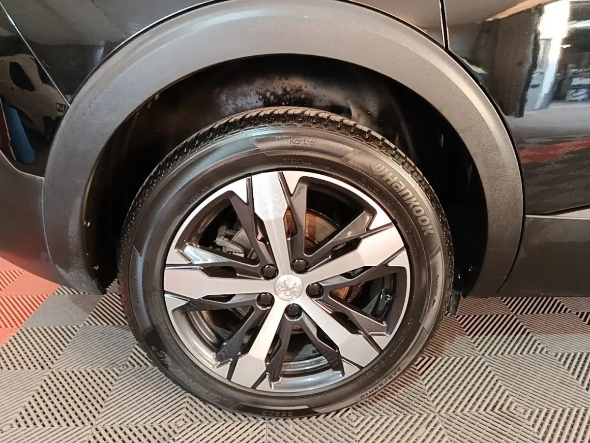 Gros plan sur la roue avant droite noire du Peugeot 5008 2018 avec jante alliage bicolore et logo lion central.