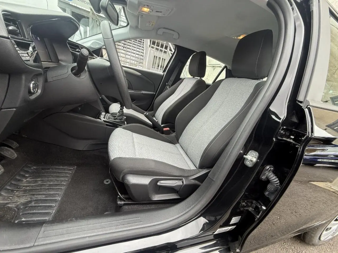 Vue intérieure côté conducteur de l’Opel Corsa noir karbon 2025, montrant les sièges tissu gris et noir et le tableau de bord.