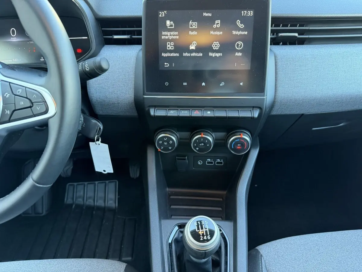 Vue intérieure centrée sur la console centrale et volant de la Renault Clio bleu, avec levier de vitesses manuel et écran tactile.