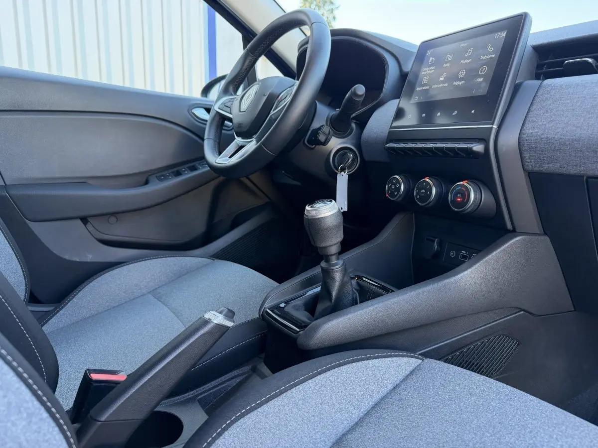 Vue intérieure côté conducteur de la Renault Clio Evolution TCe 90 2024, avec volant cuir, écran tactile et sièges gris.